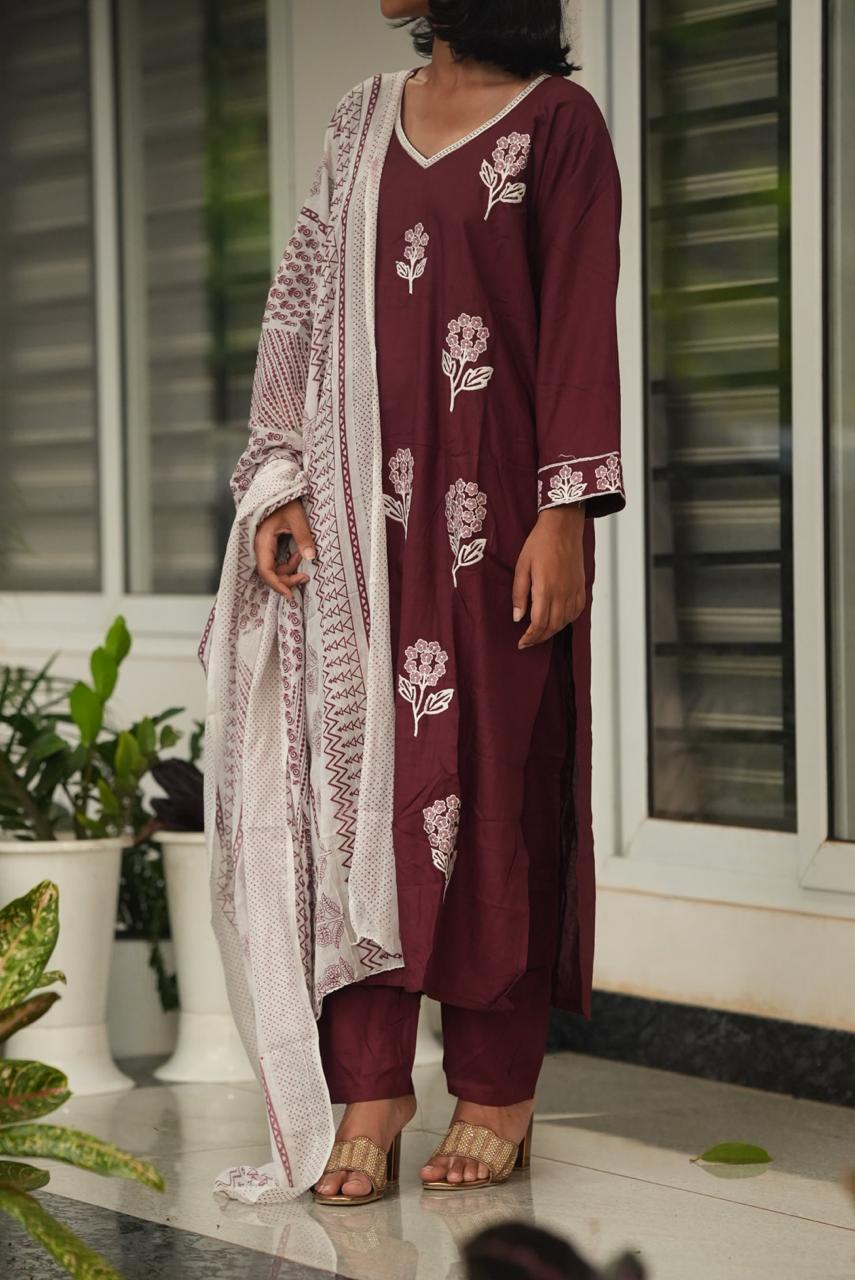 Woman wearing a maroon floral outfit with a white lace dupatta indoors.